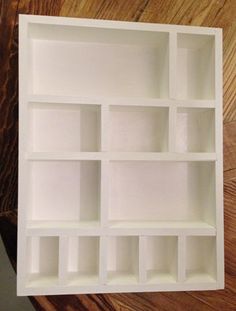 an empty white shelf with several compartments on top of it, sitting on a wooden surface