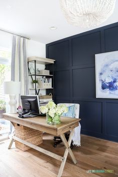 a home office with dark blue walls and wood flooring in the living room, along with a white chandelier