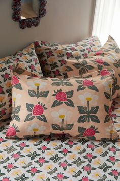 a bed topped with lots of pillows next to a window covered in pink and green flowers