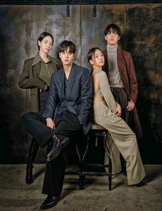 three people sitting on a chair in front of a dark background, one person is wearing a suit and the other two are standing