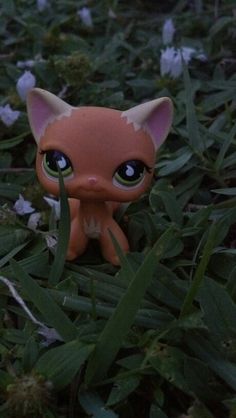 a small toy cat sitting in the grass with flowers around it's head and eyes