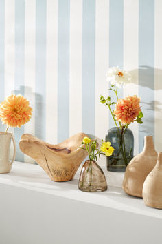 several vases with flowers in them sitting on a shelf next to striped wallpaper