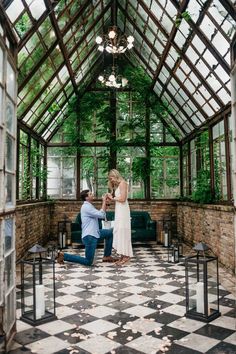 a man kneeling down next to a woman in a room with lots of windows and greenery