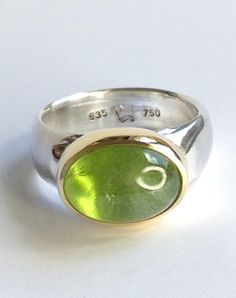 A magical peridot set in 18kt yellow gold on a 935 silver ring band. This beautiful peridot is a fresh spring green and has a wonderful vibrant look. The ring band tapers slightly towards the inside for a comfortable fit. In size 56 (inner diameter 17.8 mm), the ring is available immediately - for all other sizes, the specified shipping time applies. Size/Dimensions/Weight: Total weight: 11.4g Stone size: 14 x 10 mm / 8.6 ct. Ring band width: 8.2 - 6.2 mm Used material: peridot 935 silver 750 go Modern Peridot Rings For Anniversary, Modern Green Peridot Jewelry, Classic Round Peridot Emerald Ring, Classic Peridot Green Rings, Classic Green Peridot Ring, Green Polished Peridot Jewelry, Green Peridot Jewelry With Polished Finish, Oval Peridot Hallmarked Ring, Polished Peridot Ring