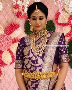 a woman in a purple and gold bridal outfit posing for the camera with flowers behind her