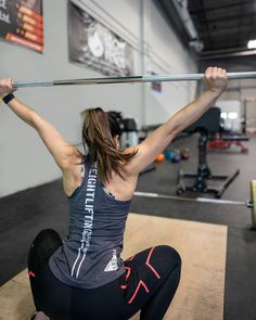 a woman squats on the floor with a bar in her hands and holds up one arm