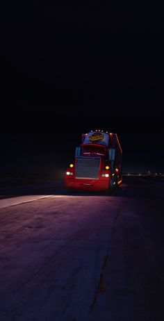 a red bus driving down a street at night with its lights on and the headlights turned on