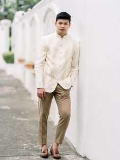 a man leaning against a white wall with his hands in his pockets and shoes on