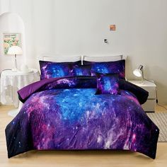 a bed covered in purple and blue galaxy comforter sets with pillows on the side