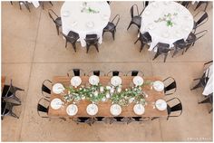 an overhead view of tables and chairs with white tablecloths, greenery and candles on them