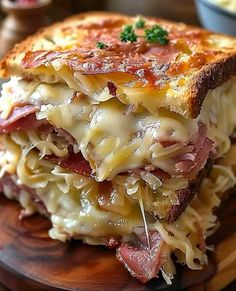 a close up of a sandwich with meat and cheese on a wooden plate next to a bowl of macaroni and cheese