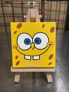 a yellow and brown cartoon character painted on a wooden easel with blue eyes, smiling