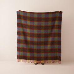 a brown and blue plaid blanket with tassels on the bottom, sitting against a white wall