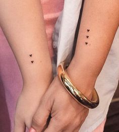 two people holding hands with small black hearts on their wrist tattoos, one has a gold bracelet