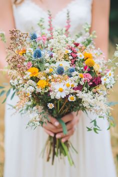 a woman in a white dress holding a bouquet of wildflowers and other flowers