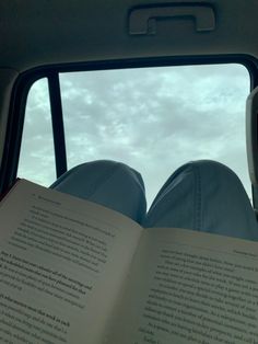 someone is reading a book while sitting in the back seat of a car on a cloudy day