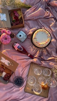 an assortment of desserts and pastries on a pink sheet covered tablecloth with wine glasses