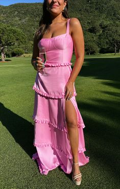 a woman in a pink dress holding a wine glass and posing for a photo on the grass