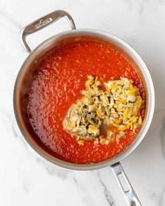 a pot filled with red sauce on top of a white counter next to a spoon