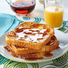 two pieces of french toast on a plate with syrup and orange juice in the background