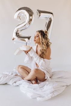 a woman is sitting on the floor eating cake and balloons are in the air behind her