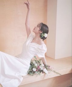 a woman in a white dress sitting on top of a wooden bench next to flowers