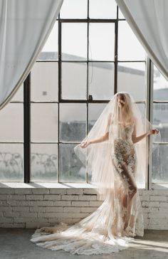 a woman in a wedding dress is standing by a window with her veil over her head