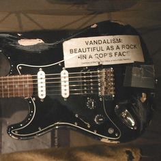 a black electric guitar is on display in a room with a sign that says, vandalism beautiful as a rock in a cop's fac