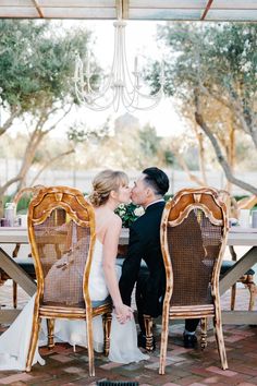 a bride and groom kissing in front of a dining room table with wicker chairs