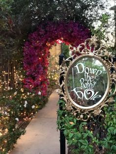 a clock that is sitting in the middle of some bushes and trees with lights behind it