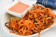 a white plate topped with shredded carrots next to a bowl of dipping sauce