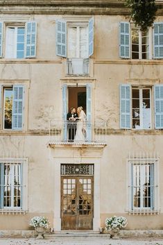 a bride and groom standing on the balcony of an old building with blue shutters