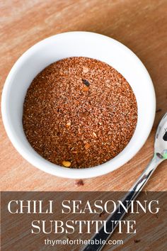 a white bowl filled with chili seasoning next to a spoon on top of a wooden table