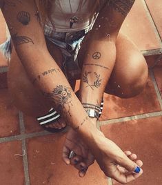 a woman sitting on the ground with two tattoos on her arms and legs, both holding hands together