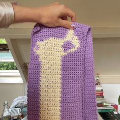 a person holding up a crocheted purple and yellow blanket