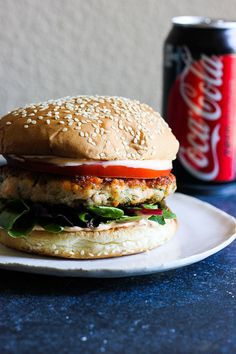 a chicken burger on a plate next to a can of coke