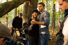 a group of people standing around each other in the woods with cameras on their laps