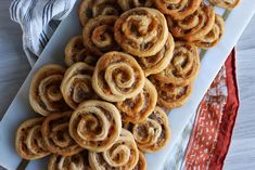 a white plate topped with cinnamon rolls on top of a red and white cloth next to a pile of doughnuts