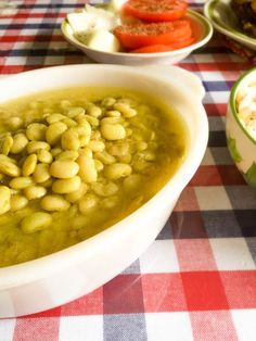 green beans in a white bowl on a red and white checkered tablecloth next to bowls of vegetables