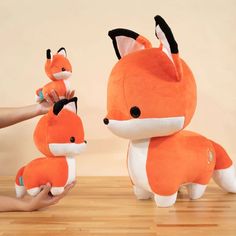 a person holding two stuffed foxes on top of a wooden table next to each other