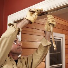 a man is working on the side of a house with wood siding and leather gloves