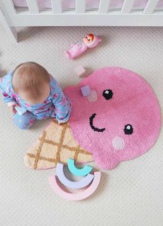 a baby playing with an ice cream cone on the floor next to a crib