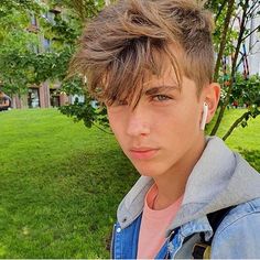 a young man with ear buds on his ears standing in front of some trees and grass