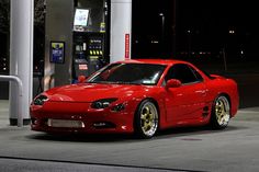 a red sports car parked in front of a gas station pump at night with its lights on