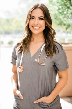 a woman in grey shirt and white scrubs standing with her hands on her hips