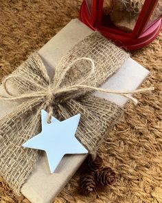 a present wrapped in burlock with a blue star on it next to pine cones