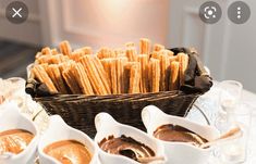 a basket full of crackers and dipping sauces on a table with glasses in front of it