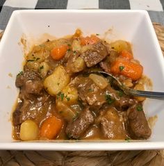 a white bowl filled with stew and carrots on top of a woven place mat