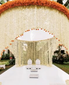 an outdoor ceremony setup with white chairs and orange flowers on the ceiling, along with draping