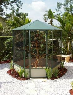 a gazebo in the middle of a garden with gravel around it and trees surrounding it